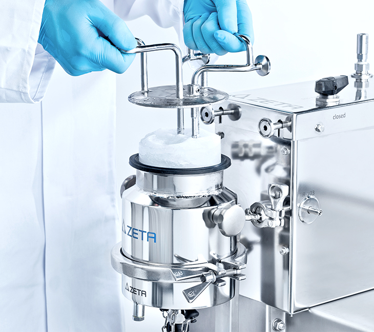 A person in a white lab coat and blue gloves is working with a shiny metal device labeled 