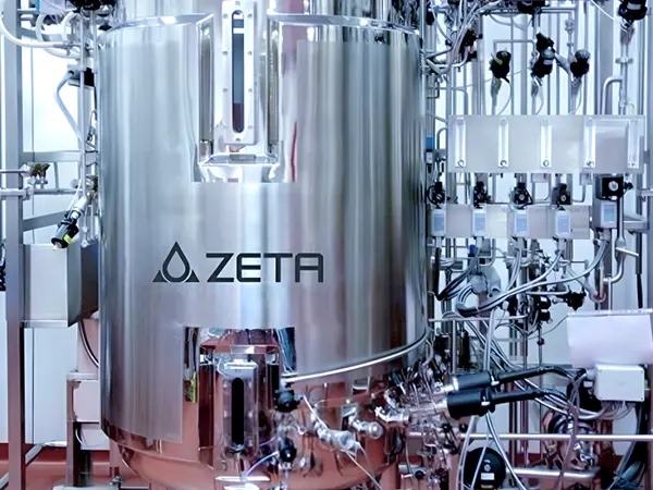 A large, shiny metal tank labeled "ZETA" is shown. It’s part of a complex industrial setup with many pipes, valves, and controls around it.
