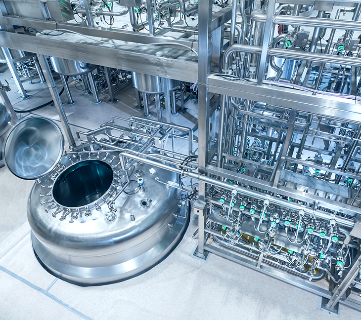The image shows a polished, stainless steel industrial setup with a large open-top cylindrical tank surrounded by pipes and valves. It’s part of a clean, high-precision processing facility.