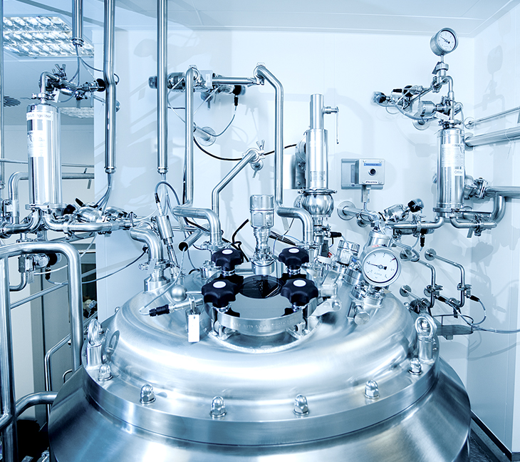 The image shows a large stainless steel vessel surrounded by pipes, valves, and gauges in a clean, technical industrial setting. It appears to be part of a controlled process system, likely used in pharmaceutical or chemical manufacturing.