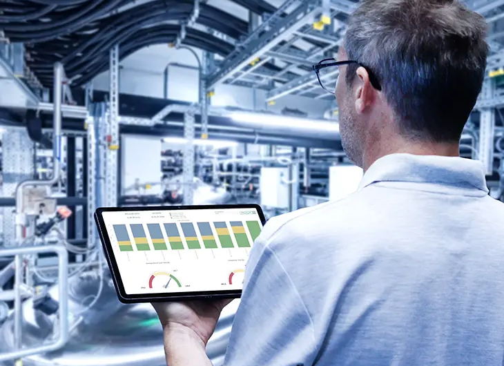 Person with tablet showing colouful charts facing production room with a lot of installations in the background