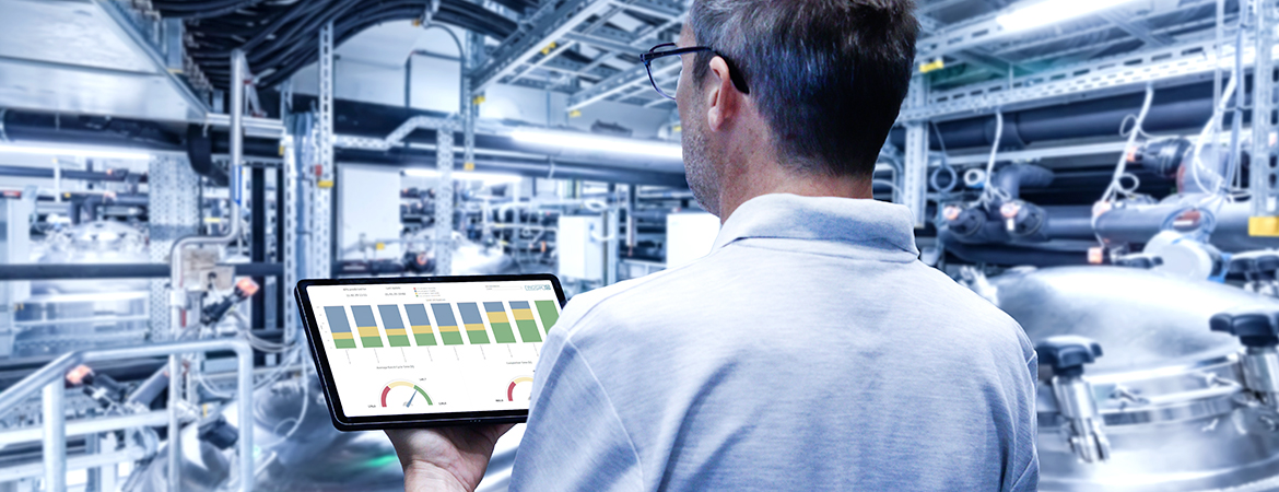 Person with tablet showing colouful charts facing production room with a lot of installations in the background